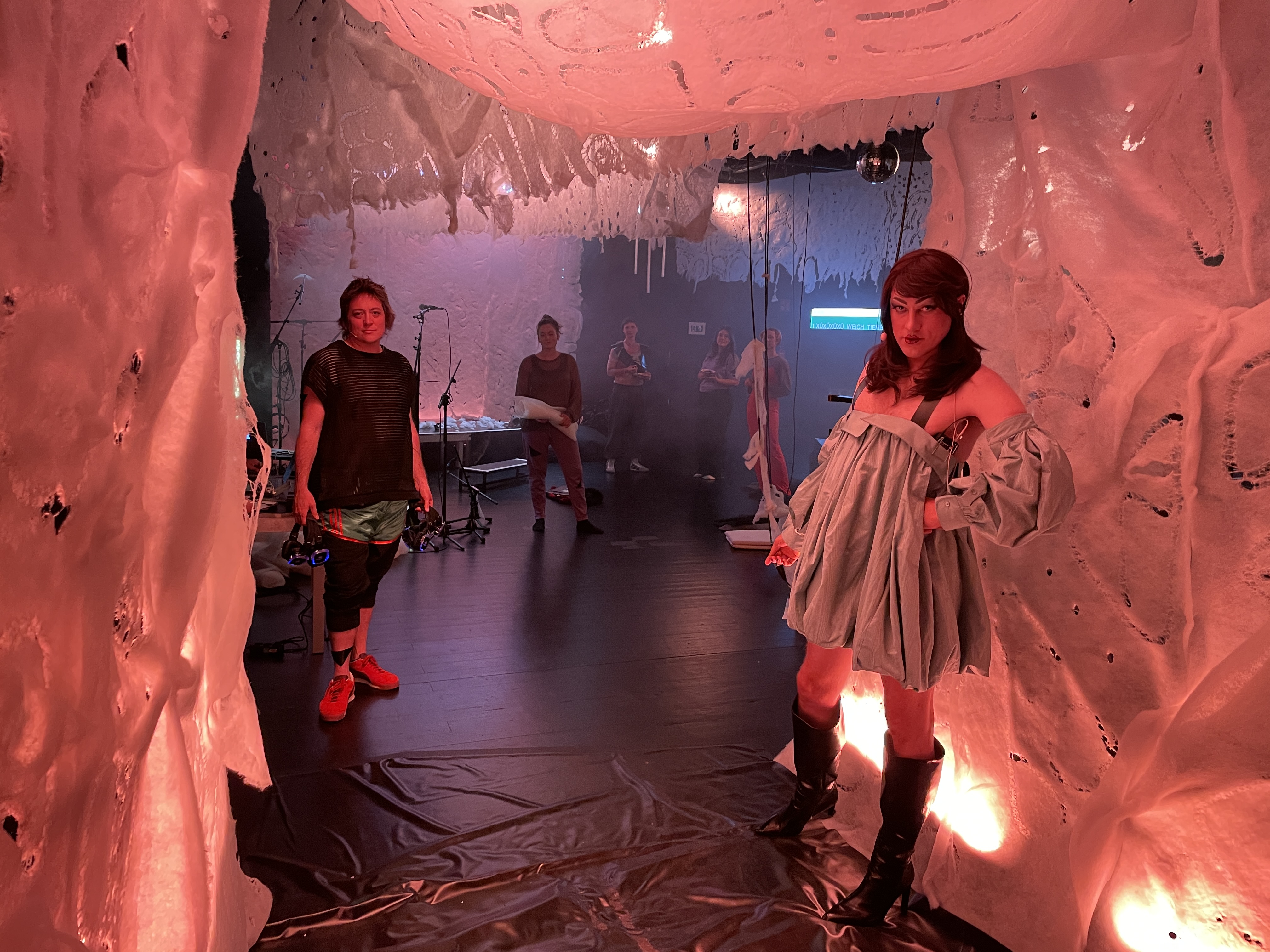 Figures stand on stage with soft white fabric around them and smoke behind them.