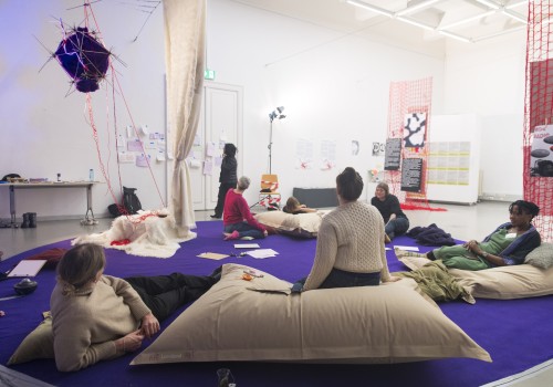 Image of a circle of people in a workshop on white pillows on a purple carpet