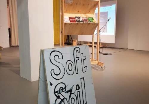 Photo of a bookshelf made of cheap plywood in a gallery and a sign with the handwritten text 