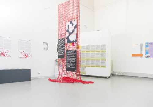 Image of an exhibition space with posters hanging from a red net and on white walls