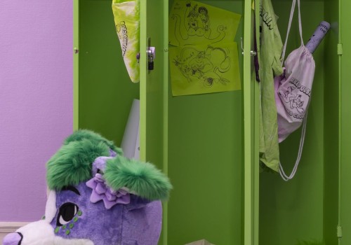 A purple mascot head sits on a green furry bench next to green lockers with messy contents.