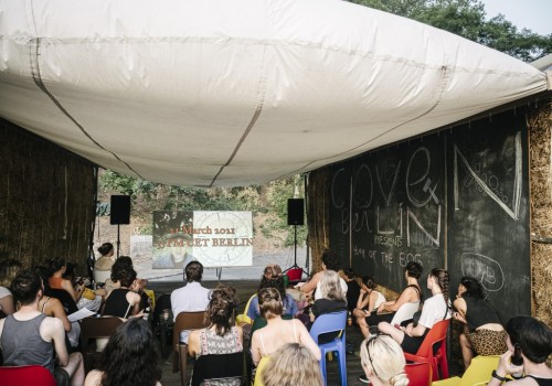 An audience sits outdoors facing a screen that says 