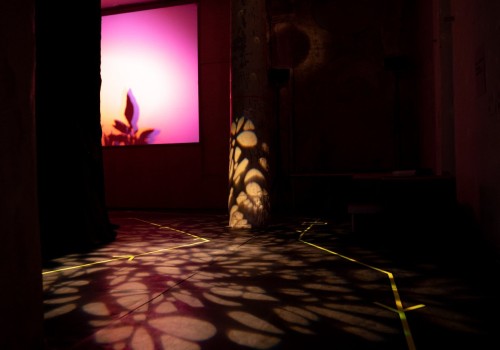 Image of a dark room. There is moody lighting, a purple light shines in the back and there are shapes of light projected on the floor.